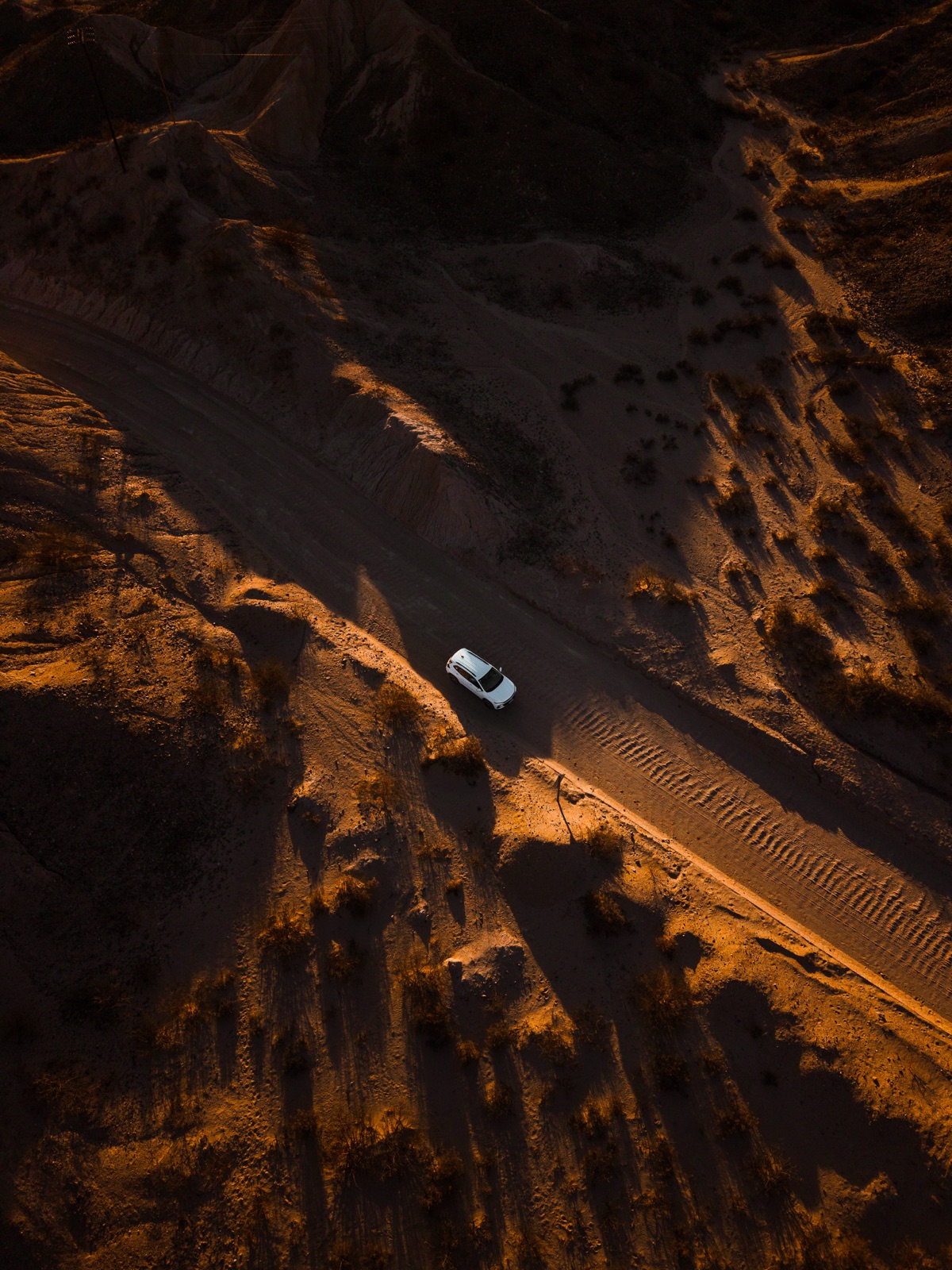 Toma aérea de una camioneta blanca en un camino entre cerros al atardecer
